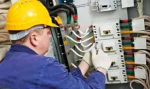a commercial electrician in a yellow hard hat repairing an industrial electrical panel with colorful wiring, emphasizing commercial electrical services in Virginia.